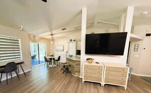 Amplia sala de estar con un televisor de pantalla plana grande, una mesa de comedor con sillas y una zona de cocina con encimera y armarios.