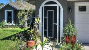 Een woonhuis met een grijze gevel, een witte deur en een klein portaal met plantenpotten.