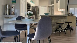 Een moderne keuken met een ronde eettafel, twee stoelen, een klein bar eiland met krukjes, en een koelkast.
