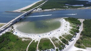 Luchtbeeld van een strand met een parkeerplaats, een brug en een wateroppervlak.