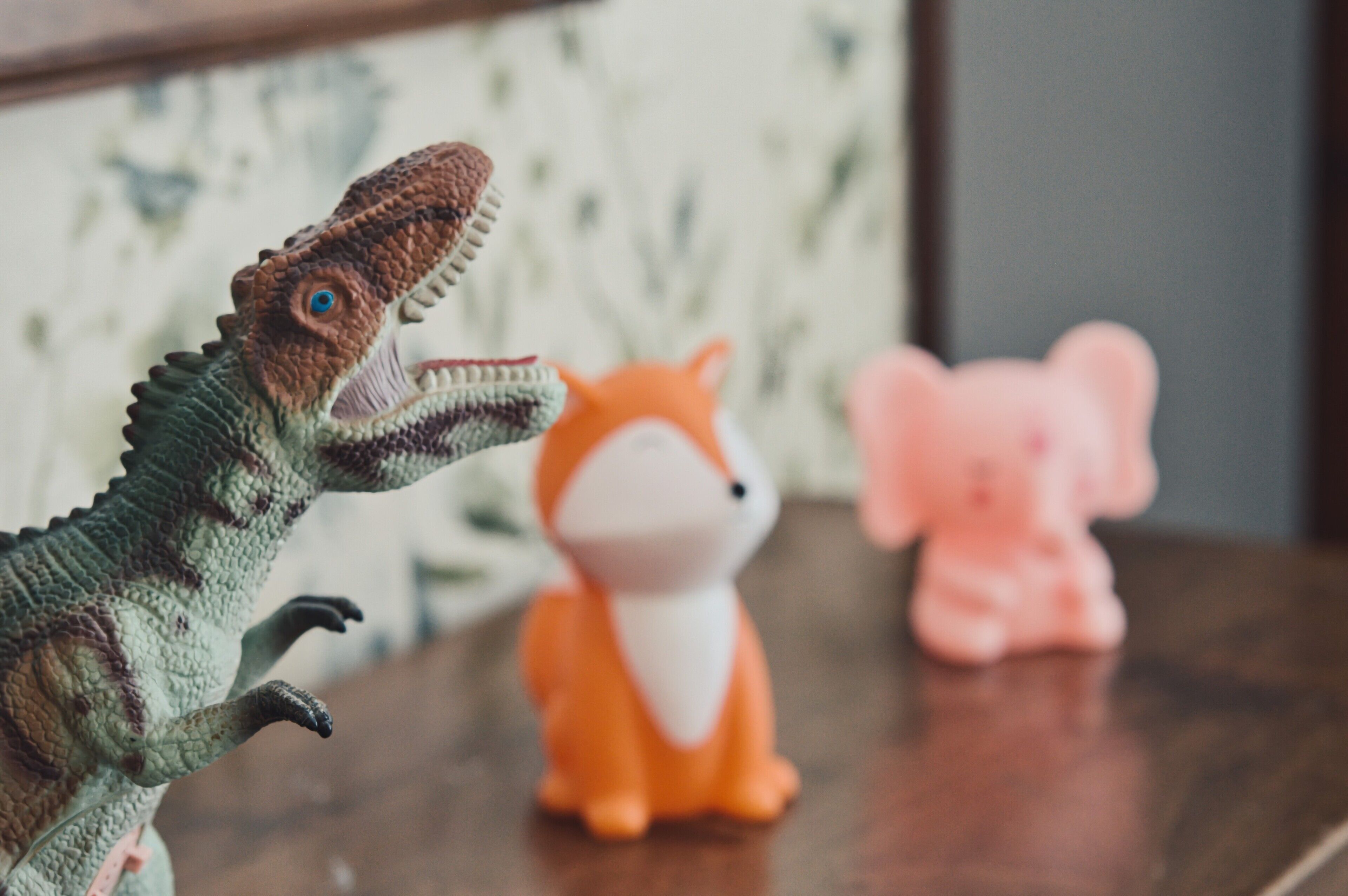 En dinosaurieleksak, en rävleksak och en spargris på en träyta.