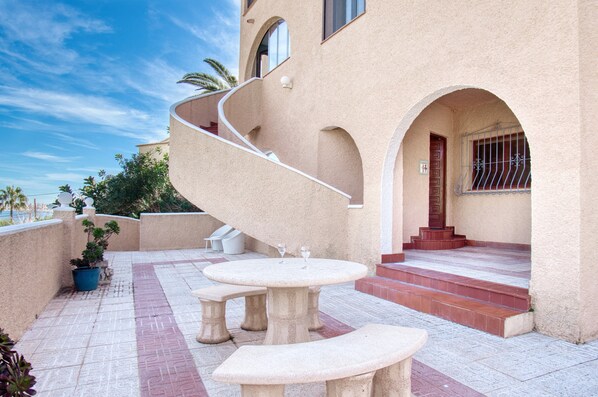 A spiral staircase leading to a door, outdoor seating with tables and benches, and a potted plant.