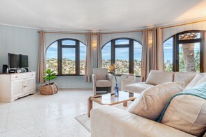 A living room with a sofa, armchair, TV, and large windows with a city view.