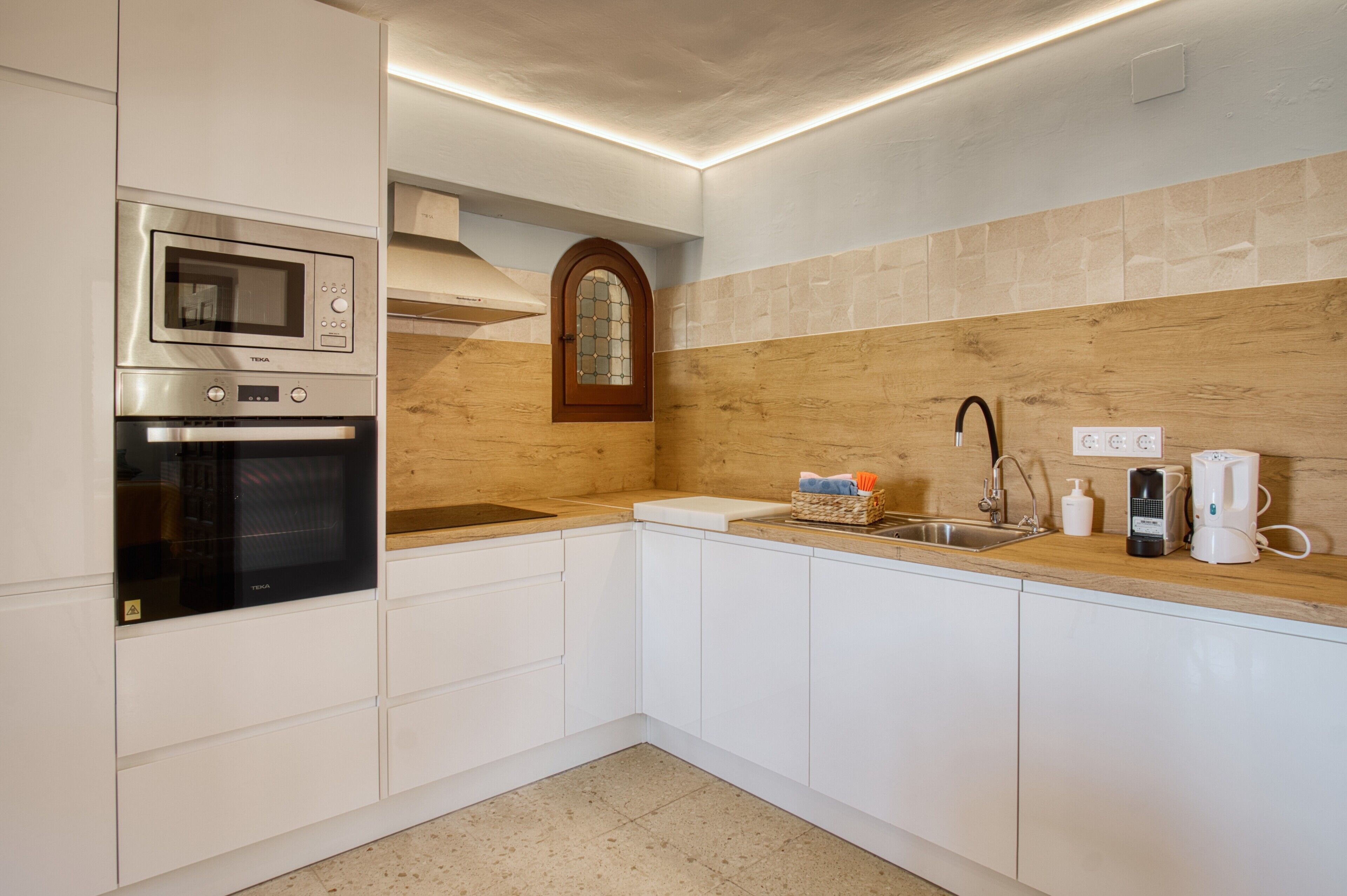 A kitchen with white cabinets, a microwave, a stove, a sink, and a wooden backsplash.