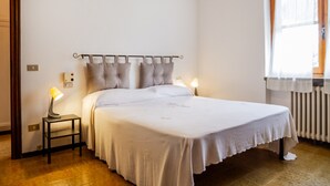 Un dormitorio con cama, lámparas de noche, un radiador y una ventana con cortinas.