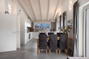 Une cuisine moderne avec des meubles blancs, une table à manger avec des chaises et une vue sur un paysage enneigé par les fenêtres.