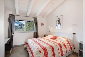 Une chambre à coucher comprenant un lit, un bureau, une chaise, une fenêtre avec des rideaux et un tableau encadré accroché au mur.