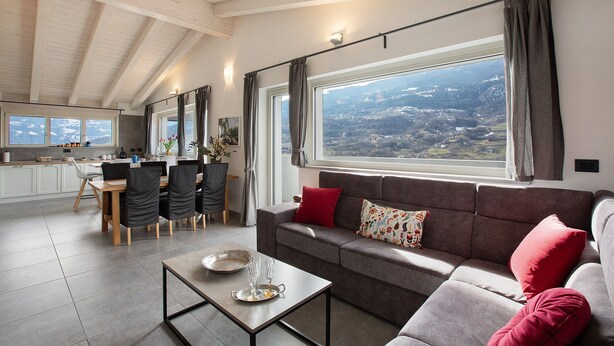 Una sala de estar moderna con sofá, mesa de comedor y sillas, un ventanal con vistas y una cocina al fondo.