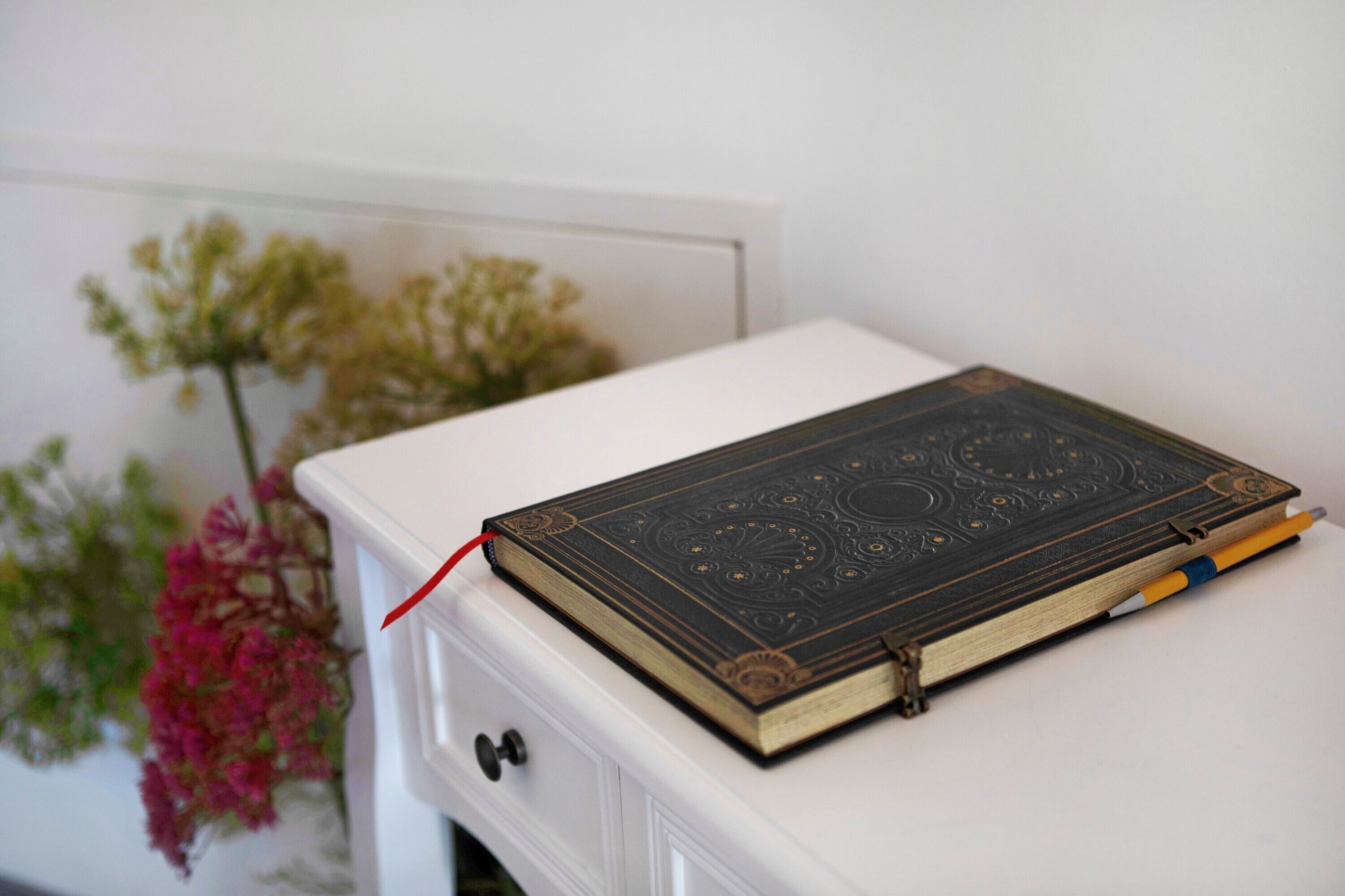 A book on a white table with a red ribbon, next to a white drawer with a knob.