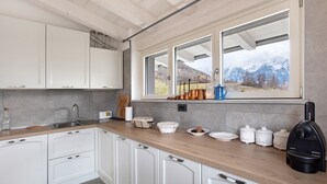 Una cocina moderna con armarios blancos, encimera de madera y ventana con vistas a la montaña.