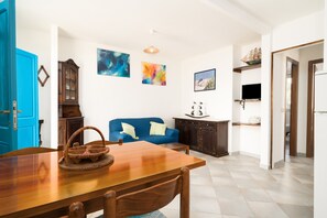 A living room with a wooden dining table, blue sofa, and a TV on a shelf.