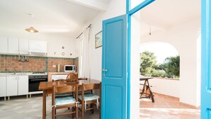 A modern kitchen with white cabinets, a microwave, and a dining area with a blue door. - Holiday Home 'Villa Maria' with Private Terrace and Private Garden (Orosei)