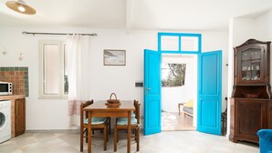 A kitchen with a washing machine, a dining table with chairs, a blue door, and a cabinet with glass doors. - Holiday Home 'Villa Maria' with Private Terrace and Private Garden (Orosei)