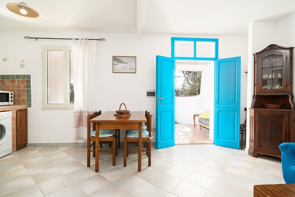A kitchen with a washing machine, a dining table with chairs, a blue door, and a cabinet with glass doors.