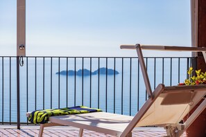 Ein Balkon mit Liegestuhl und Kissen, mit Blick auf ein Gewässer und entfernte Inseln.