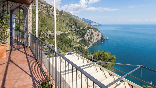 A balcony with a view of a coastal landscape, including a mountain and the sea.