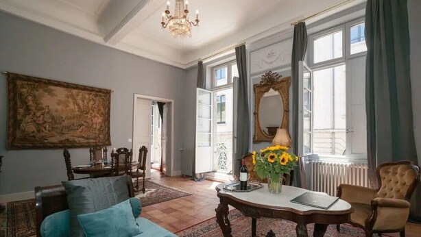 A room with a bed, a table with a vase of sunflowers, a mirror, and a chandelier.