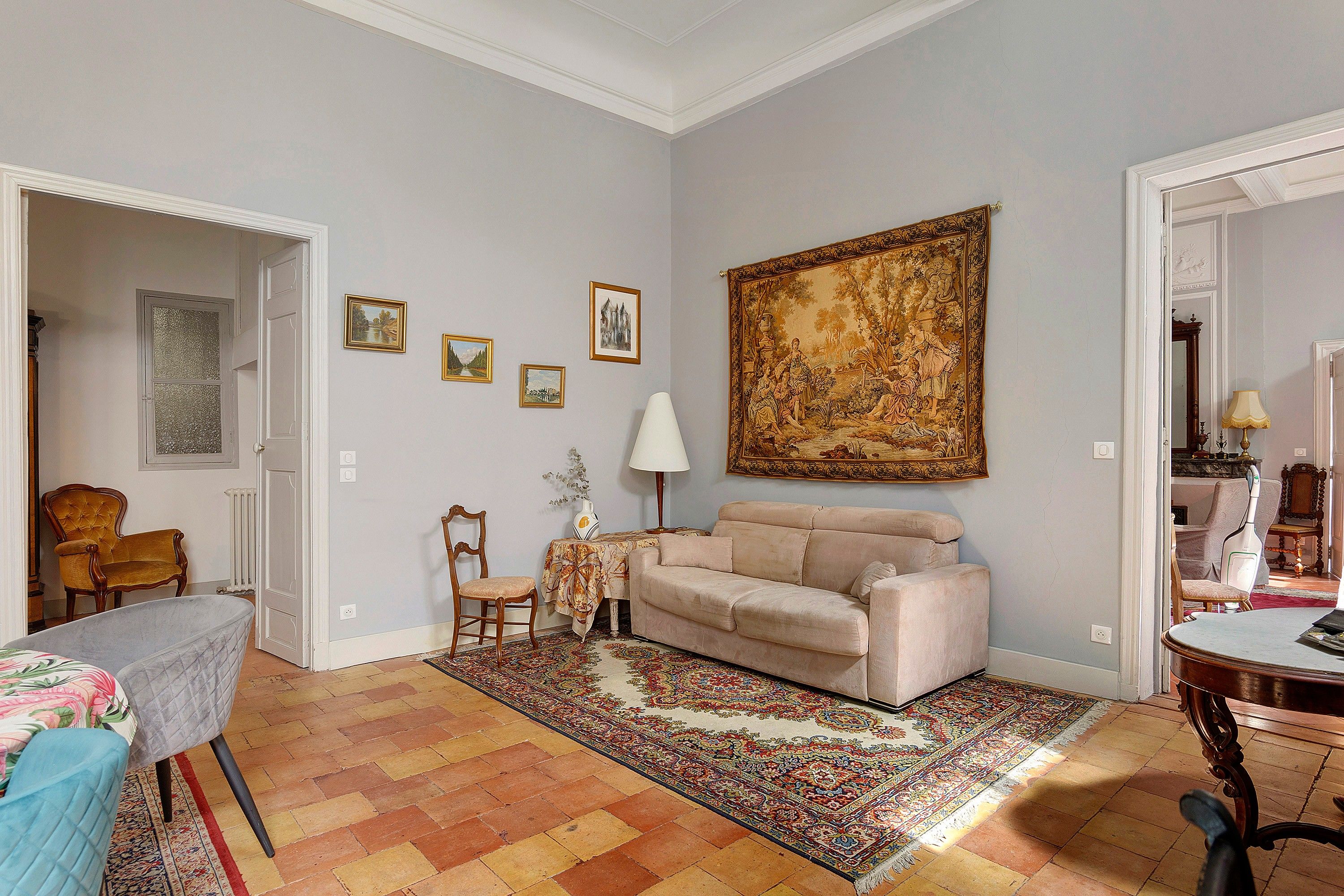 Een woonkamer met een beige bank, een kamerkleed met patroon en een groot schilderij in een lijst aan de muur.