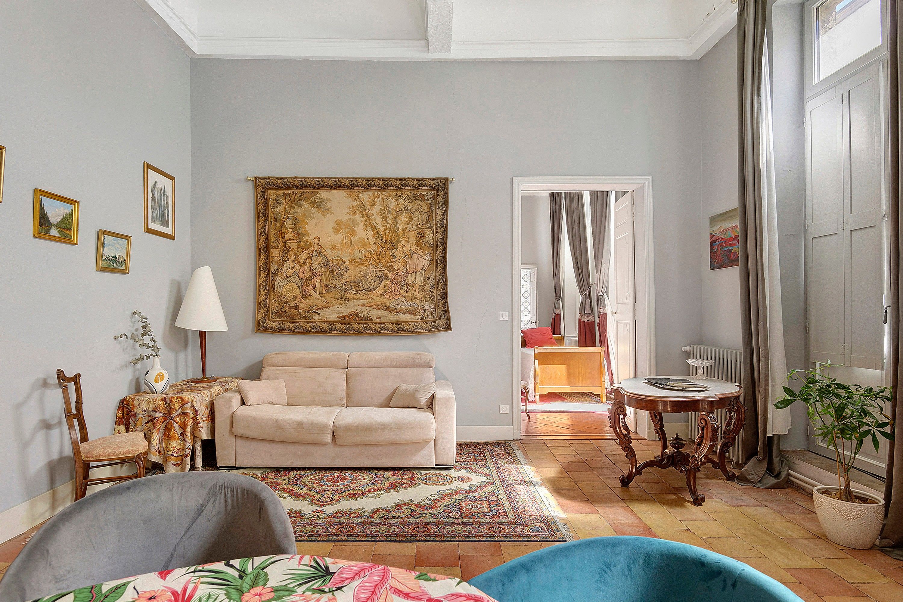 Un salon comprenant un canapé, une table basse, un fauteuil, une grande tapisserie et une plante en pot.