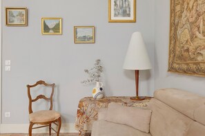 Una habitación con un sofá, una silla, una mesa con un florero y tres cuadros en la pared.