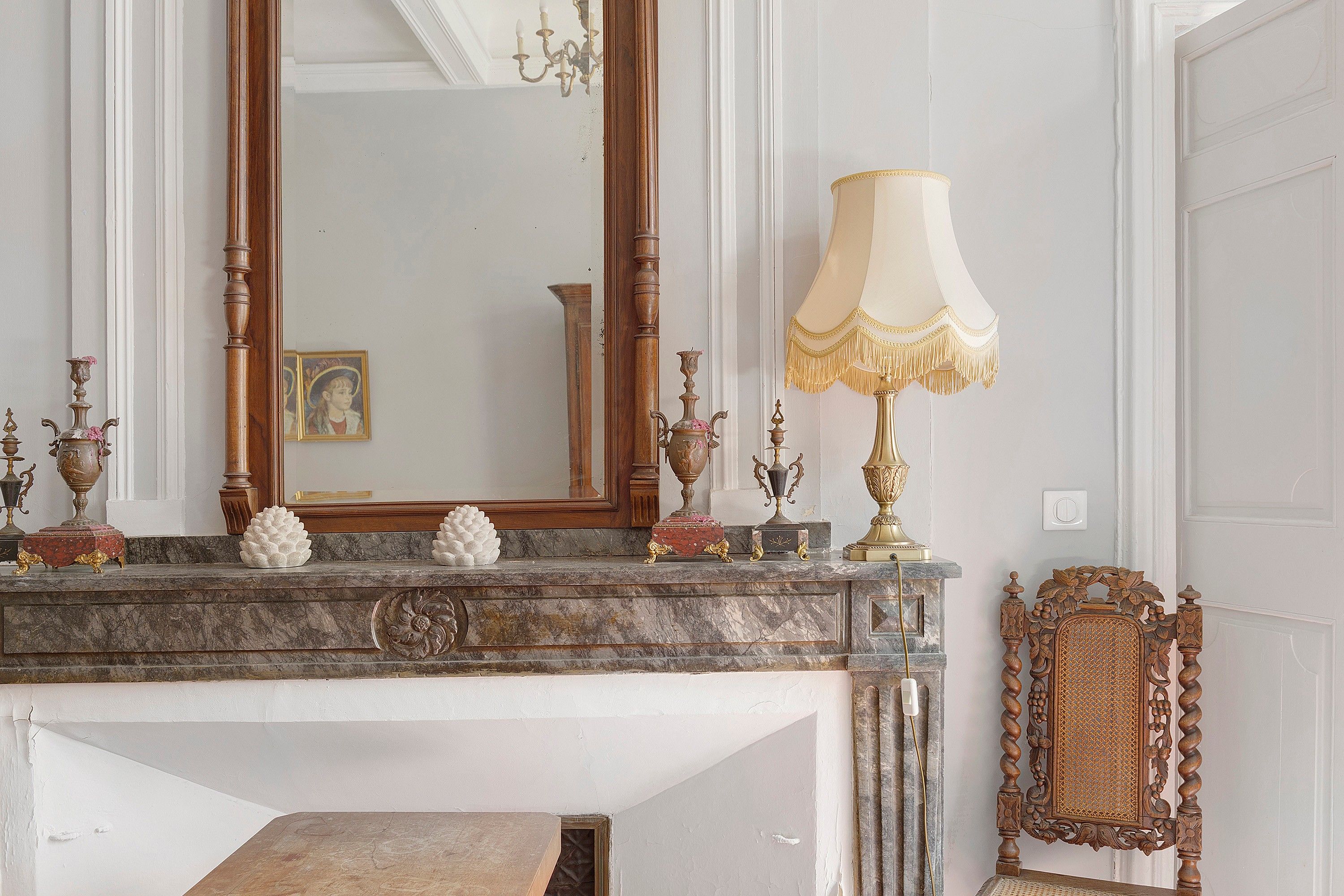 Une cheminée en marbre agrémentée de décorations raffinées, un grand miroir et une lampe classique.