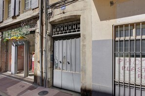 Fachada de edificio con una reja metálica cerrada, un letrero con el número 26 y una ventana con barrotes de seguridad.