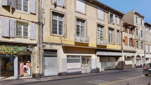 A street view with a row of buildings, some with closed shutters, and a clear sky above. - Apartment 'La Suite Barbes' with Shared Garden, Balcony and Wi-Fi (Carcassonne)