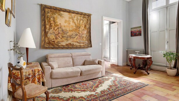 A room with a beige sofa, a patterned rug, a table with a lamp, and a large painting on the wall. - Apartment 'La Suite Barbes' with Shared Garden, Balcony and Wi-Fi (Carcassonne)