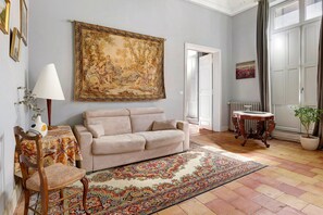 Ein Zimmer mit einem beigen Sofa, einem gemusterten Teppich, einem Tisch mit Lampe und einem großen Gemälde an der Wand.