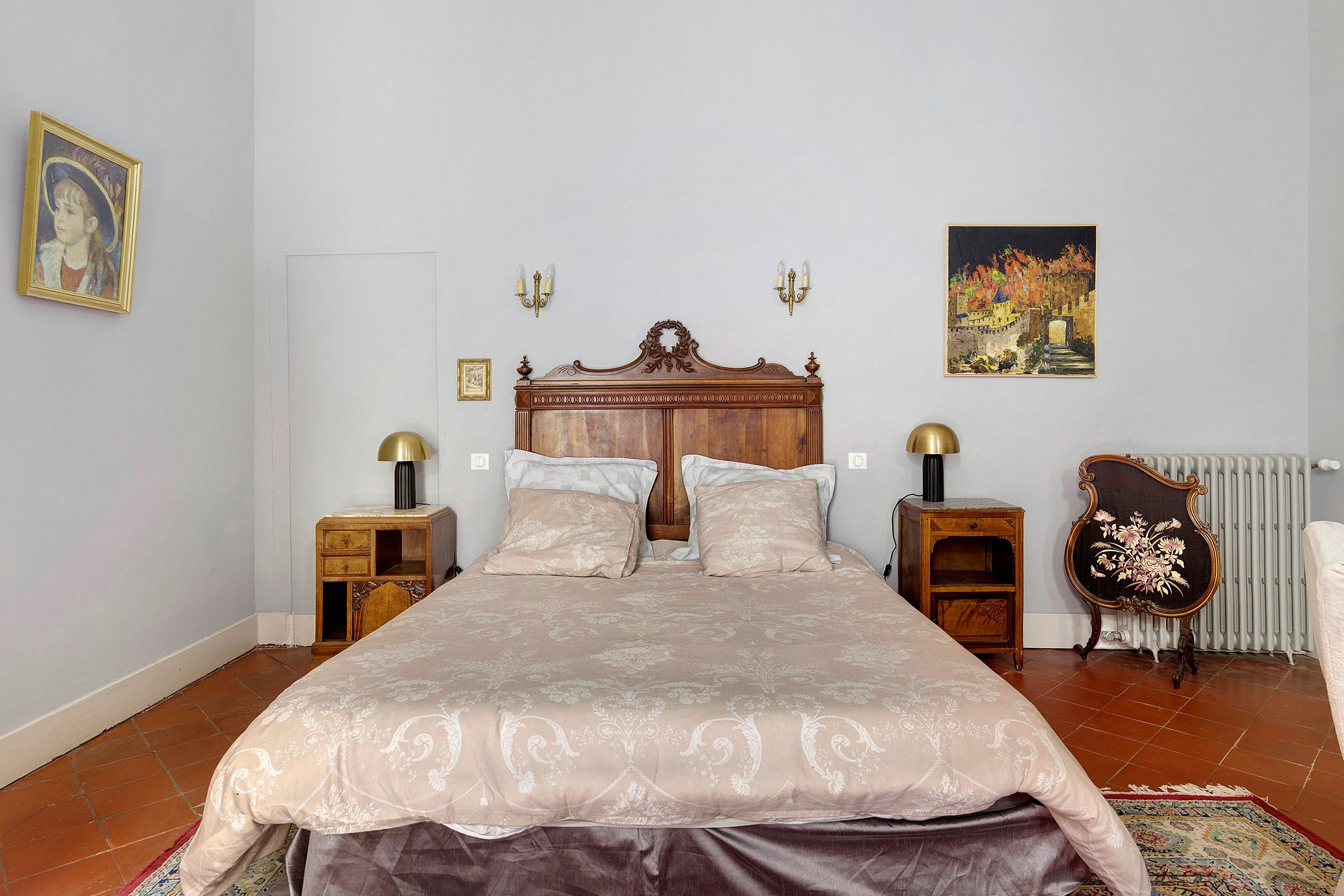 Een slaapkamer met een groot bed, twee nachtkastjes, een radiator en wandlampen.