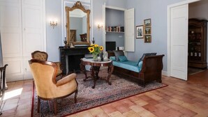 A room with a fireplace, a sofa, a chair, a table with a vase of sunflowers, and a bookshelf.