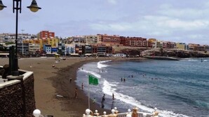 A coastal cityscape with a beach, buildings, and a flag. - Vacation Villa 'Delicias' with Sea View, Private Terrace and Wi-Fi (Taliarte)