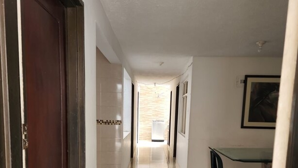 Un pasillo con suelo de baldosas, una puerta de madera a la izquierda y una mesa con sillas a la derecha.