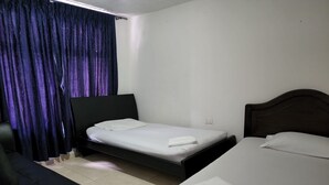 Una habitación con dos camas, un sofá negro y una ventana con cortinas moradas.