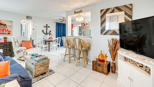 Ein Wohnzimmer mit Sofa, Sesseln, einem Couchtisch, einem Fernseher und einer Küchenzeile mit Bar.