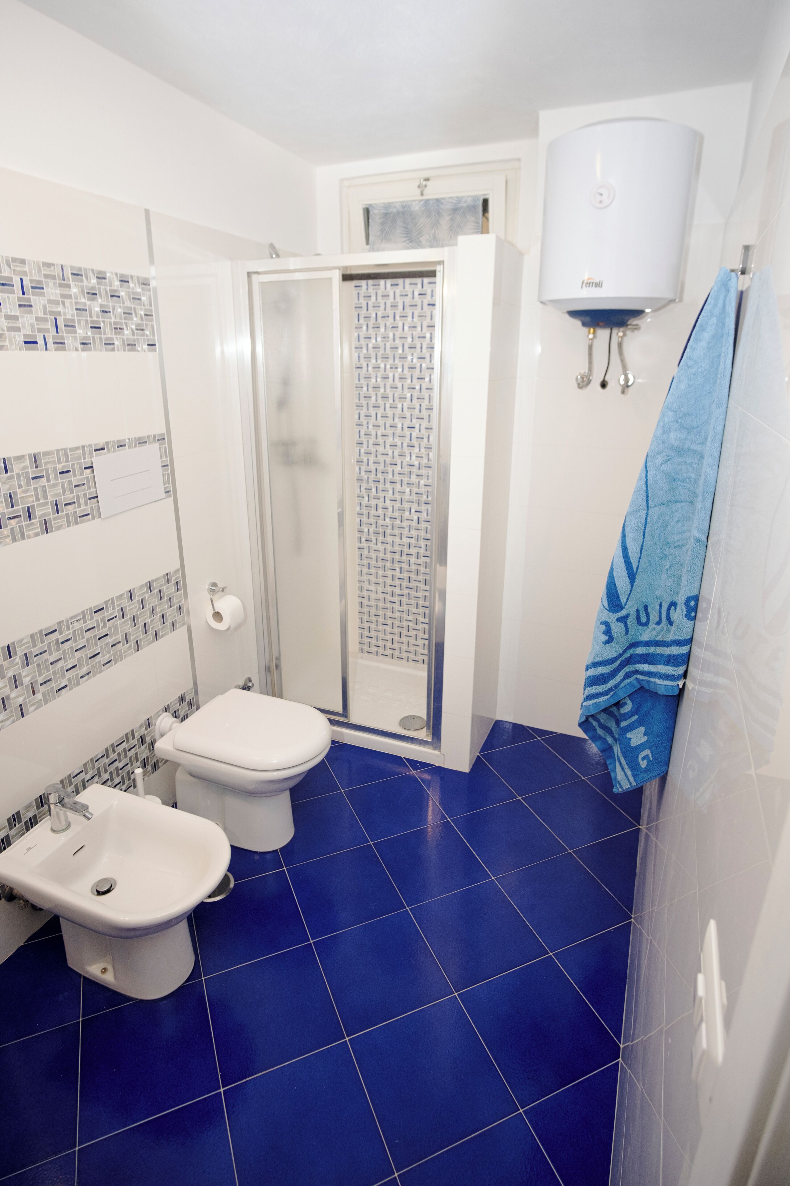 A bathroom with a shower, two toilets, a bidet, and a towel rack.