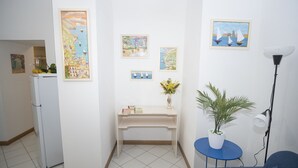 A small, clean room with a white refrigerator, a desk with a vase of flowers, and a blue chair. - De Vivo Realty - Fortuna House (Sant'Agnello)