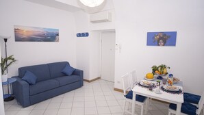 A modern living room with a blue sofa, a dining table with chairs, and a ceiling light fixture. - De Vivo Realty - Fortuna House (Sant'Agnello)