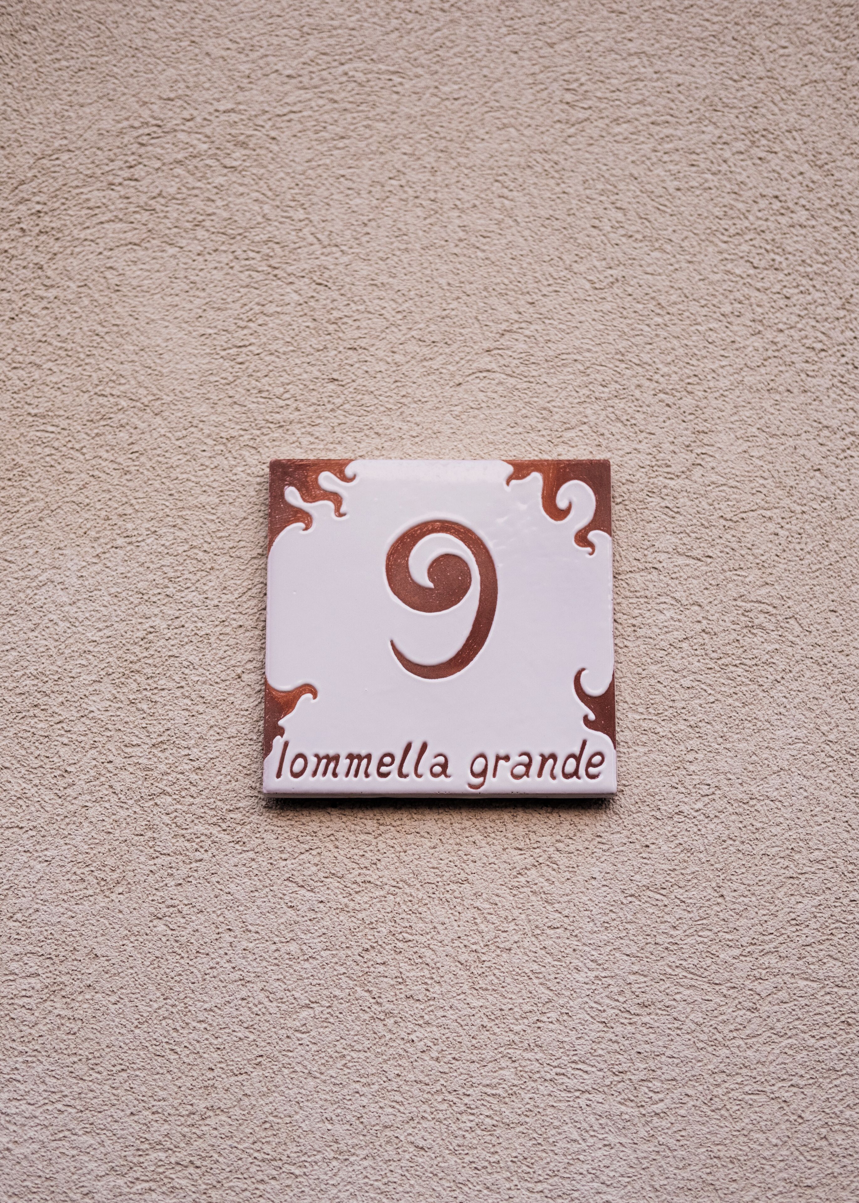 A small, square, white sign with a brown swirl design and the text "Iommella grande" on a beige carpet.