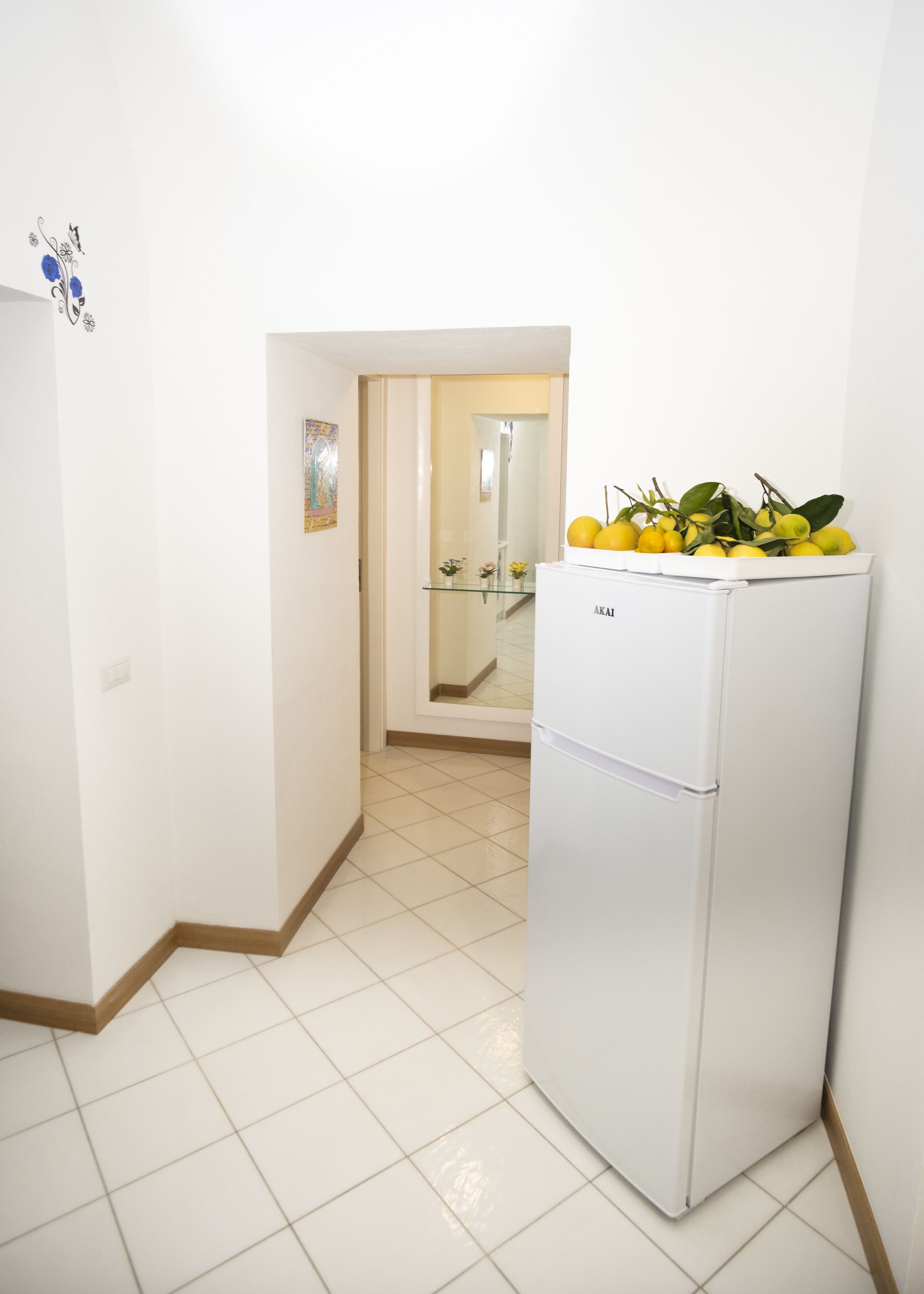 Una cocina compacta con un refrigerador blanco, un armario de vidrio con limones y piso de baldosas.