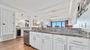 A modern kitchen with white cabinets, granite countertops, and a built-in dishwasher. - Grand Pointe 613 | Beachfront | Resort Amenities | MyBeach Getaways (Orange Beach)