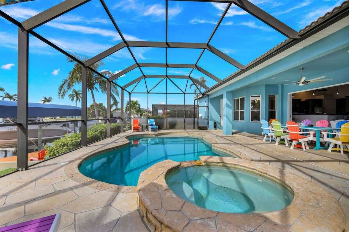 A covered outdoor swimming pool with a patio area, a ceiling fan, and colorful chairs.