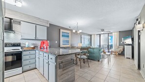 A modern kitchen with granite countertops, a built-in oven, and a dining area with a table and chairs. - BEACHFRONT, TWO POOLS, PRIVATE BALCONY! (Orange Beach)