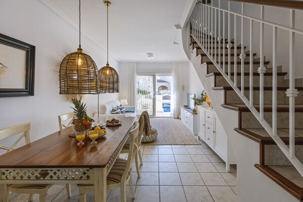 A dining area with a wooden table, chairs, and hanging light fixtures. A staircase is visible to the right.