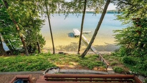 A wooden deck with a grill, overlooking a lake with a dock and boat. - Spacious Waterfront Home on Long Lake (Traverse City)