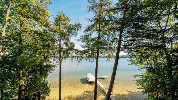A boat docked at a clear lake surrounded by trees. - Spacious Waterfront Home on Long Lake (Traverse City)