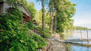 A lakeside cabin with a wooden deck and stairs leading to a porch. - Spacious Waterfront Home on Long Lake (Traverse City)