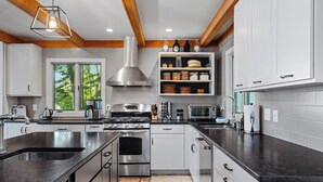A modern kitchen with stainless steel appliances, white cabinetry, and a wooden ceiling. - Spacious Waterfront Home on Long Lake (Traverse City)