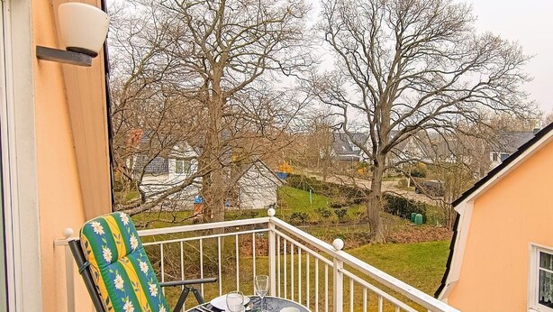 A balcony with two chairs and a table, overlooking a residential area with trees and houses. - Ferienwohnung F18 - 2-zi. Fewo im Dachgeschoss für 3 Personen mit Wlan (Graal-Müritz)