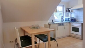 A small kitchen with a dining table, chairs, a microwave, a coffee maker, and a stove. - Ferienwohnung F18 - 2-zi. Fewo im Dachgeschoss für 3 Personen mit Wlan (Graal-Müritz)